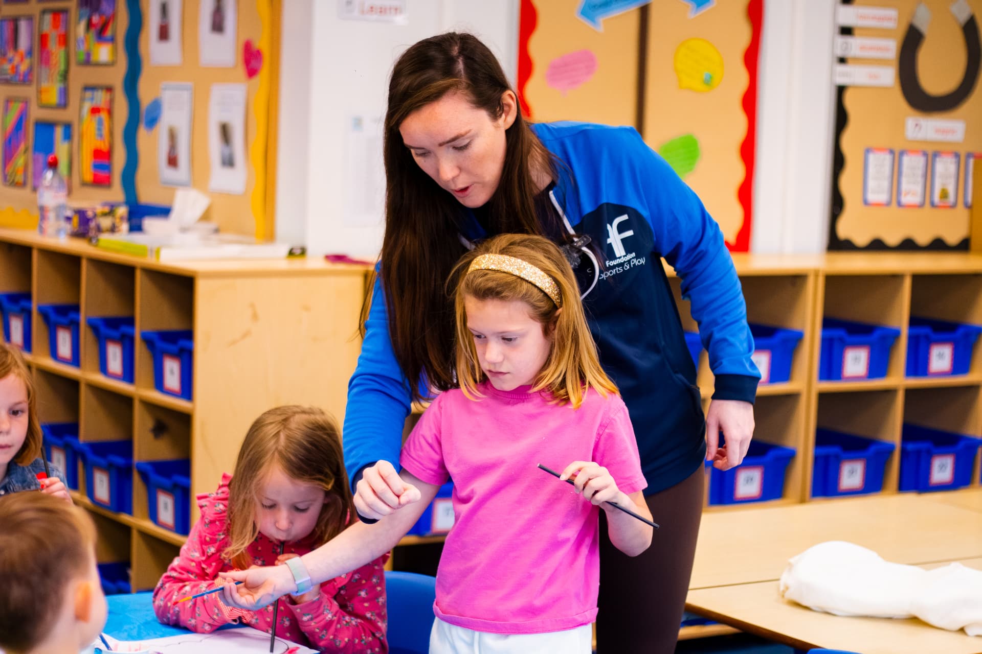 Foundation coach supporting children with a painting activity in a classroom